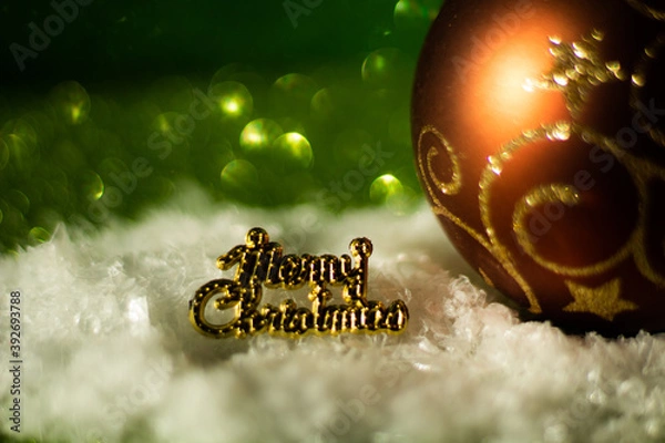Obraz Merry Christmas - simple concept with decorative Christmas ball, text and snow, green glitter background, selective focus, free copy space