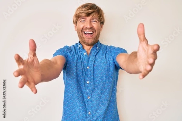 Fototapeta Young blond man wearing casual clothes looking at the camera smiling with open arms for hug. cheerful expression embracing happiness.