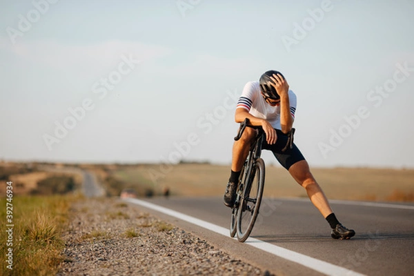 Fototapeta Exhausted cyclist relaxing on road after long riding