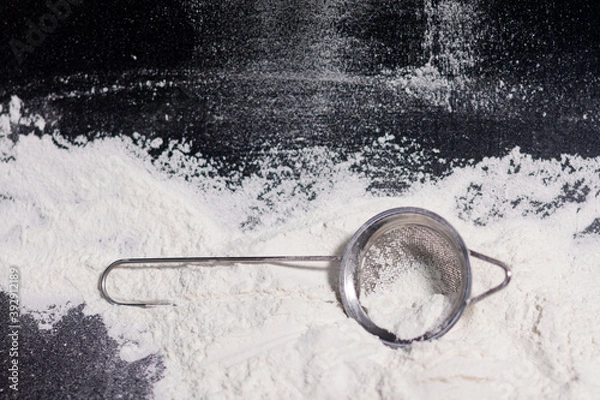 Fototapeta A metal sieve with a handle next to it on a mound of flour.