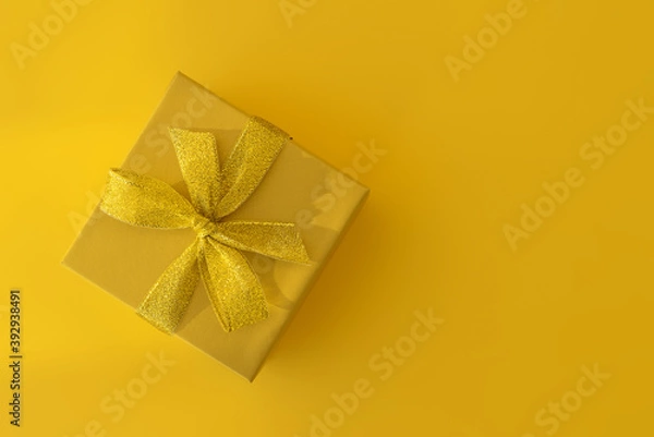 Obraz Yellow gift box with a gold ribbon on a yellow background. Gift for birthday, Christmas, mother's Day, Valentine's Day. Top view, horizontal position, copy space
