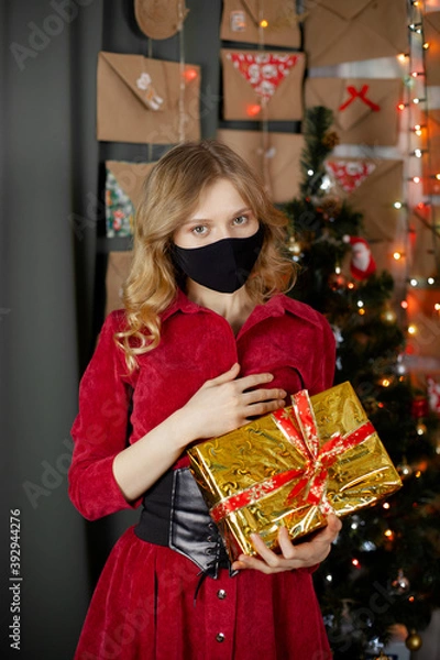 Fototapeta Portrait of a beautiful girl in medical mask, standing in front of decorated christmas tree at home