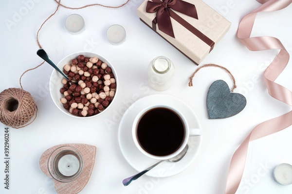 Fototapeta Holiday background with gift box, coffee Cup, cereal plate, ribbon, candles and hearts on a light background. The view from the top. Concept February 14.