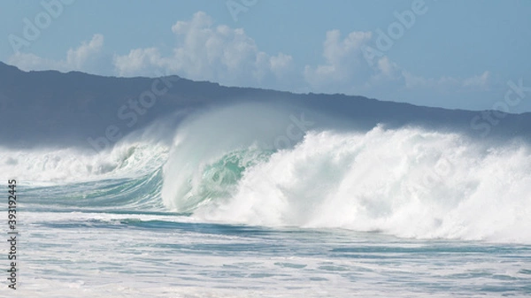 Fototapeta Breaking waves against the backdrop of a ridge and a cloudy sky. The beach is located on the North Shore of the Island of Oahu.