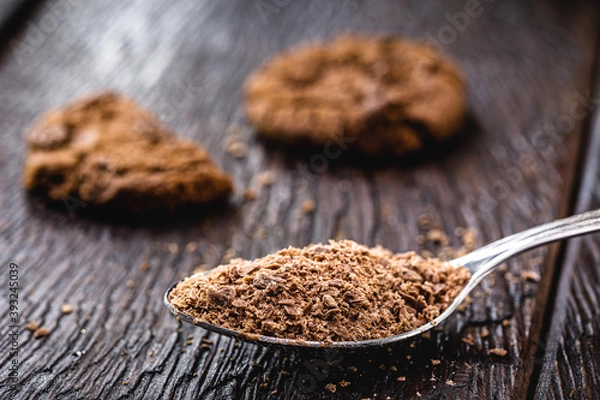Obraz spoon with grated chocolate, chocolate powder used as an ingredient in sweets. Homemade chocolate chip cookies in the background