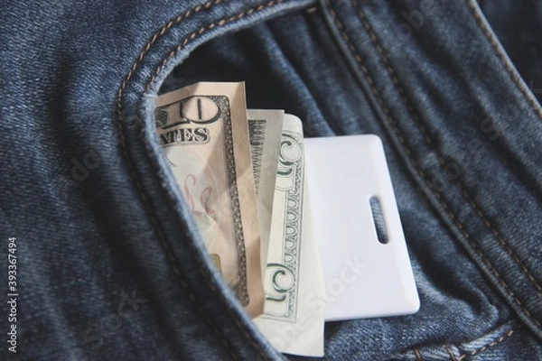 Obraz Money and card key in a pocket of blue jeans of office employee hurrying on a lunch break close up.