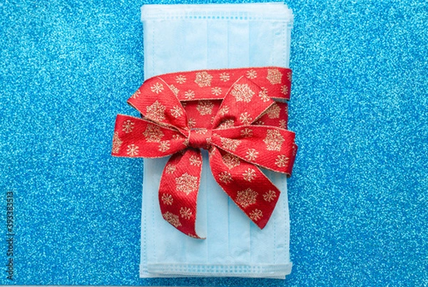 Obraz medical protective face masks as a gift with a red ribbon on a classic blue background. Christmas and New Year 2021 decor. Holidays self-isolation and coronavirus pandemic concept