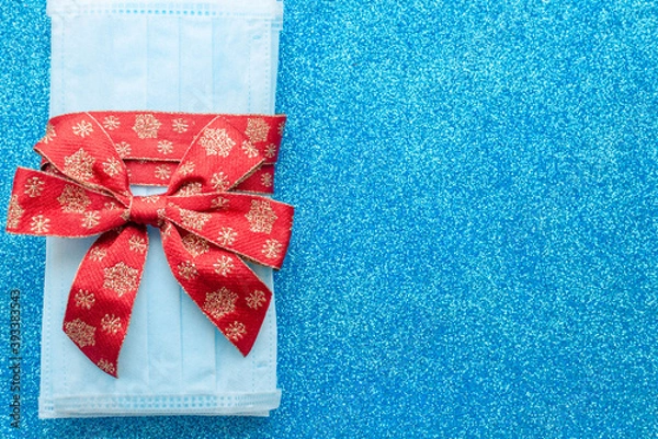 Obraz medical protective face masks as a gift with a red ribbon on a classic blue background. Christmas and New Year 2021 decor. Holidays self-isolation and coronavirus pandemic concept
