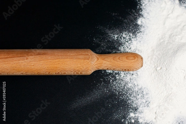 Fototapeta To the right, on the dark surface of the table, is a mound of white flour. In the center is a rolling pin.