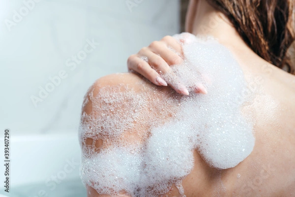 Fototapeta Close-up of a female shoulder in foam. The girl takes a bath with foam. Body care, skin care, asparagus procedures