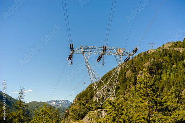 Obraz Power lines and tower passing through mountains.