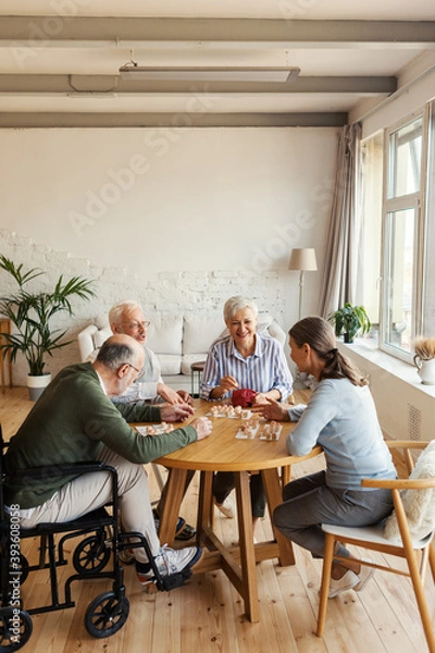 Obraz Group of four friendly senior people, two men and two women, sitting at table and enjoying playing bingo game in nursing home