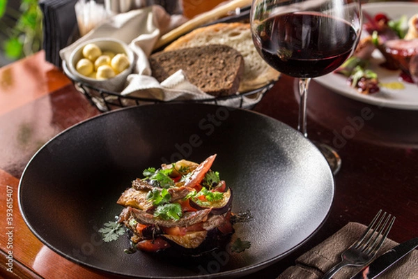 Fototapeta Warm salad with grilled veal, tomato, eggplant and glass of red wine on the table at restaurant