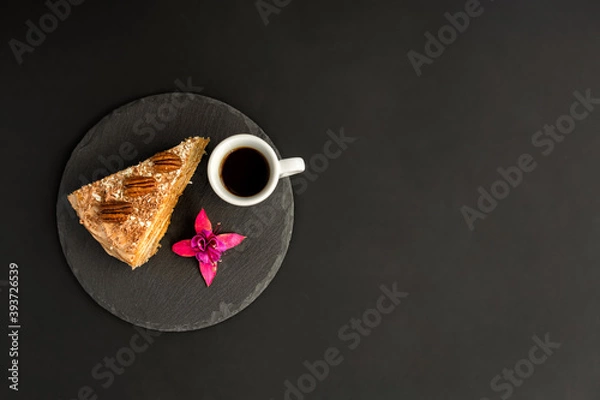 Obraz A typical Portuguese cake made of cookies called Bolo de Bolasa with cream, pecans, black and white chocolate on a black slate with espresso and a flower on a black background. Flatlay. Copy space