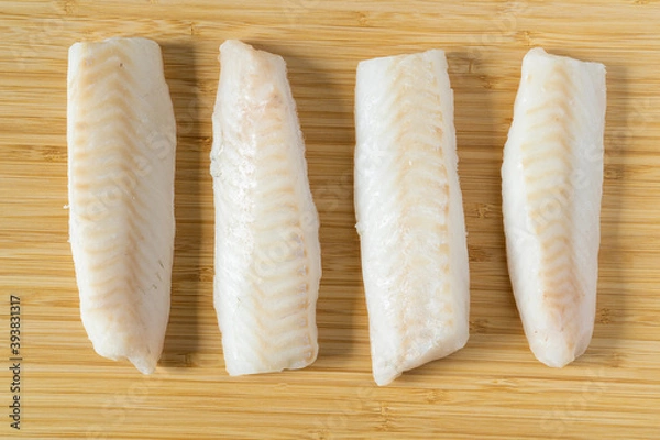Fototapeta Fresh iced pieces of cod fish loins or fillets on wooden cutting board. Top view.