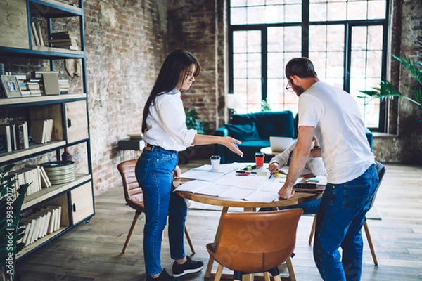 Obraz Focused colleagues doing paperwork and talking in modern spacious workspace