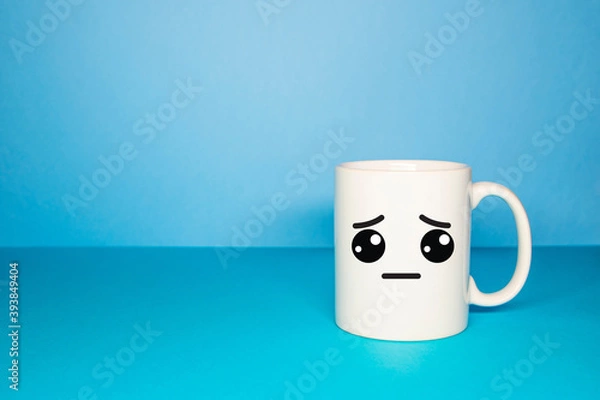 Fototapeta Close-up of a white mug on a blue background looking sad. Concept of sadness caused by Covid-19, new normal and Blue Monday.