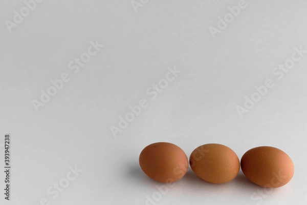 Fototapeta three brown eggs lie in one row on a white background
