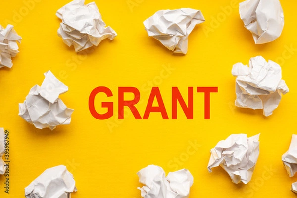 Fototapeta Grant text on yellow background with copy space. Crumpled sheets of paper lie around. Business concept image