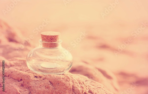 Obraz A beautiful empty pot-bellied glass bottle of an unusual shape stands on the beach stones close-up in the pink rays of the sunset. Wallpaper postcard welness banner. Free space for text