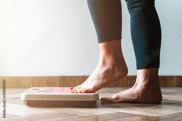 Fototapeta Female checking kilogrammes getting on the scale - self care and body positivity concept - warm flare on left