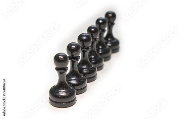 Fototapeta Wooden chess pieces. Black pawns stand behind each other looking out from behind their comrades on a white background