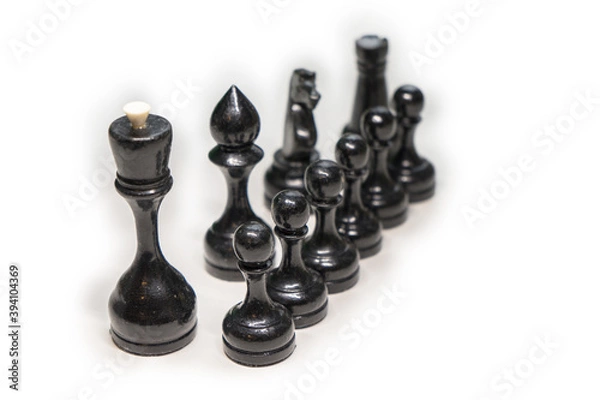 Obraz Wooden chess pieces. black pawns stand one after another, looking out from behind their comrades on a white background, focus on the second row of pawns, next to their main comrades, king, Bishop, kni