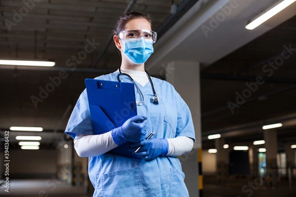 Obraz Medical EMS worker wearing PPE uniform,safety goggles and face mask,holding clipboard at mobile test center site,PCR Coronavirus COVID-19 virus disease detection in drive-thru check & control facility