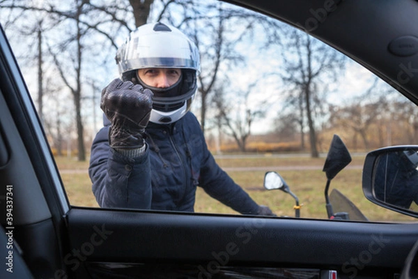 Fototapeta Angry motorcyclist knocking with fist in glove in car side window, view from inside