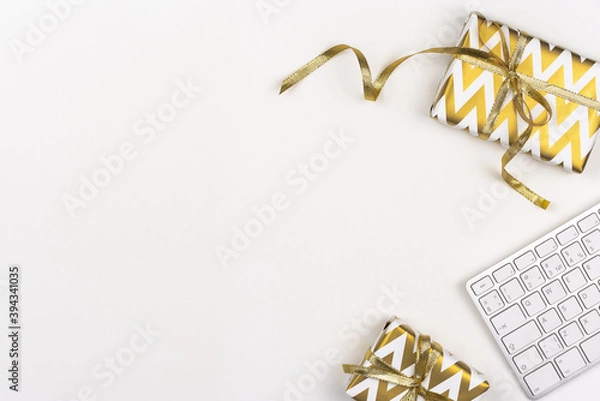 Fototapeta Christmas gift in decorated box with golden ribbon and keyboard on white background. Business concept. Copy space. Top view of presents on work table.