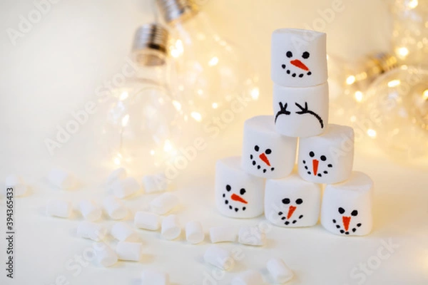 Fototapeta team of marshmallow snowmen on a beige background in the lighting of a garland