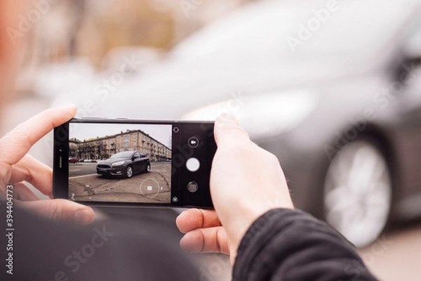 Obraz a man takes pictures of a car on the phone in the middle of the city