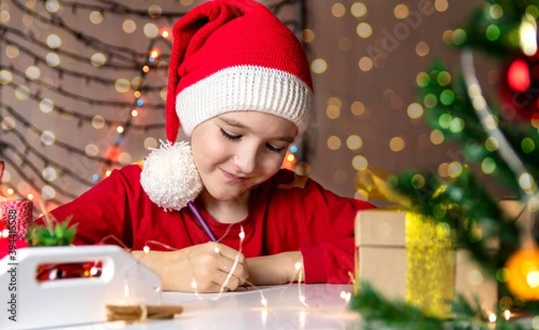 Obraz Boy in a red Christmas hat writes a letter to Santa Claus
