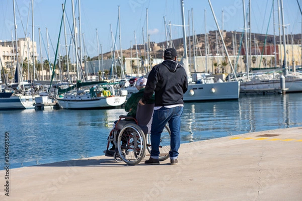 Obraz a man walks with an old man in a wheelchair