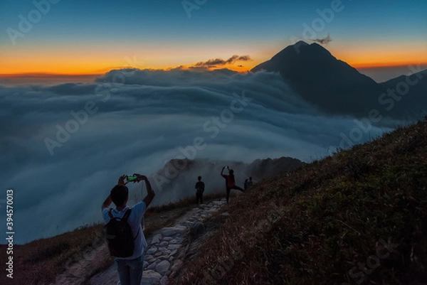 Fototapeta Hiker taking photo of Mountain Fung Wong Shan - Lantau Peak from Sunset Peak at dusk. Natural landmark in hong kong