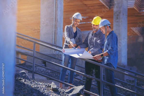 Fototapeta Structural engineer and architect working with blueprints discuss at the stairway, outdoors building construction site.