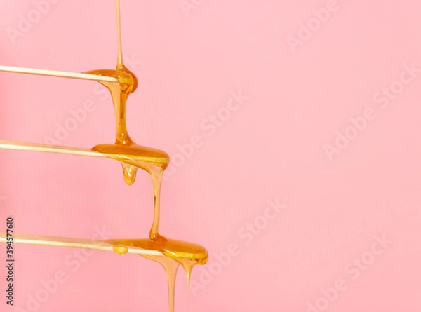 Obraz Sugar paste for hair removal runs down a wooden spatula. The concept of depilation, waxing and sugaring. Pink background, free space for text.