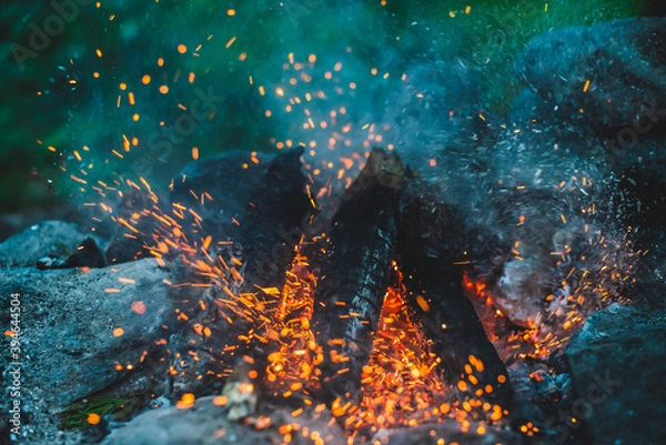 Fototapeta Vivid smoldered firewoods burned in fire close-up. Atmospheric background with orange flame of campfire. Full frame image of bonfire. Warm whirlwind of glowing embers and ashes in air. Sparks in bokeh