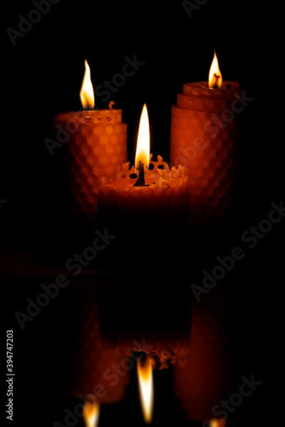 Fototapeta Close-up of three small yellow candles on a black background.