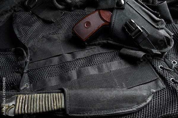 Obraz A knife in a scabbard and an air pistol in a holster on a black unloading vest, top view