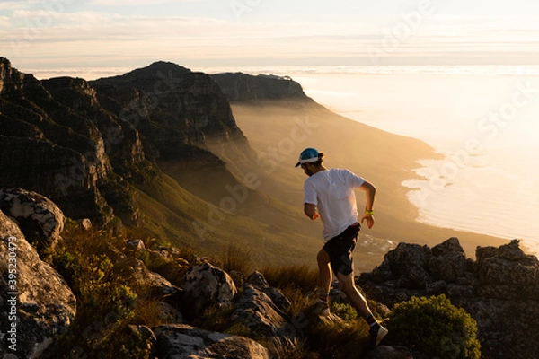 Fototapeta A person running along a mountain top at sunset 