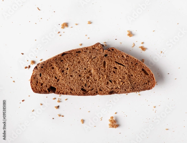 Fototapeta Slice of brown bread with crumbs on white background. Flat lay.