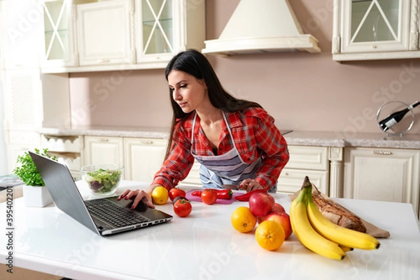 Obraz girl in the kitchen watching a recipe in a laptop