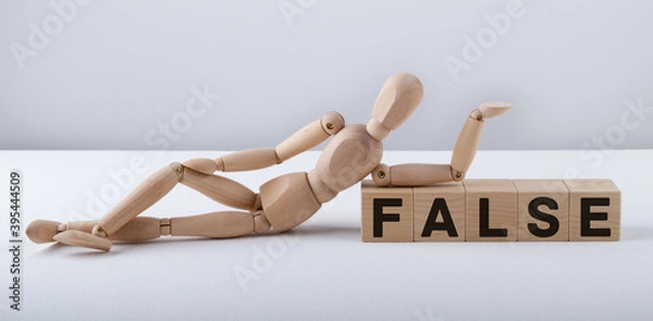 Obraz Wooden man sits on wooden cubes with the text FALSE.