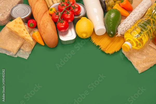 Obraz Different groceries or food donations on green background with copyspace - pasta, fresh vegatables, canned food, baguette, cooking oil, tomatoes, cheese. Food bank or food delivery concept