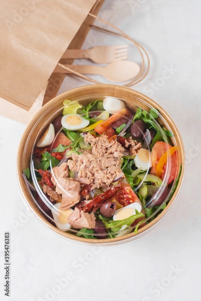 Fototapeta Fish diet salad with tuna, tomatoes, arugula on light background. Healthy vegetarian lunch. Concept eco restaurant delivery, environment protection. Take away food in brown paper craft plate.