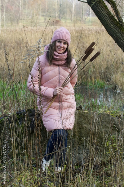 Obraz A girl in autumn clothes with a bouquet of reeds in her hands. Walking in nature in the park.
