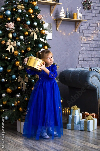 Obraz Happy little girl holding gift box by christmas tree Isolated.