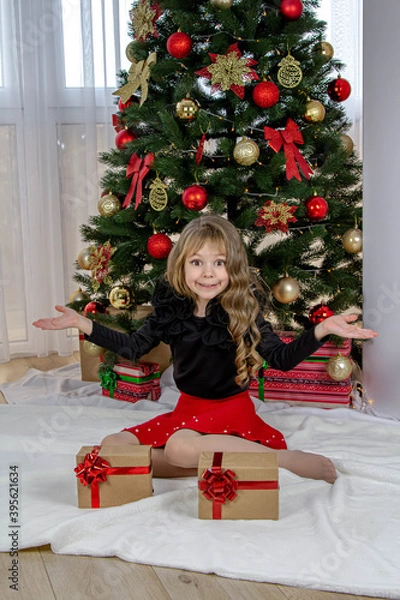 Obraz A beautiful little girl stands before the choice of a small or large gift for the New Year and Christmas. The girl decides which gift to choose