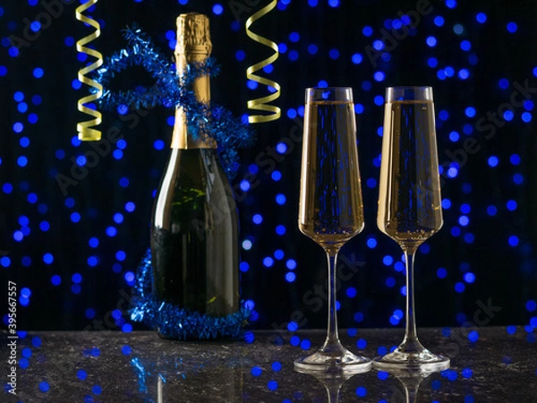 Fototapeta Decorated champagne bottle and two filled glasses on a blue bokeh background.